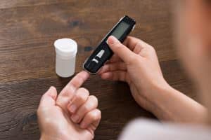 Close-up Of Person Hands Holding Glucometer For Measuring Blood Sugar At Desk