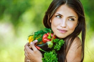 Portrait of young beautiful woman with bare shoulders holding a vegetable - parsley, pepper, eggplant, on green background summer nature.