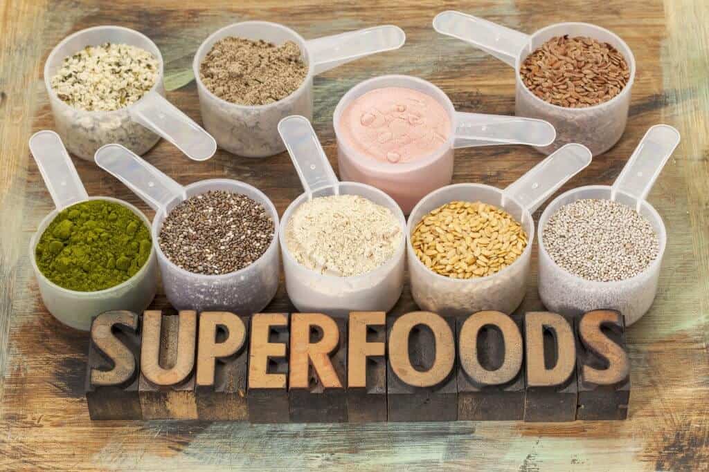 superfoods word in letterpress for the omad diet in wood type with plastic scoops of healthy seeds and powders (chia, flax, hemp, pomegranate fruit powder, wheatgrass, maca root)