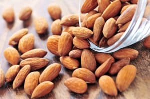 Raw almonds spilling out of small glass bowl