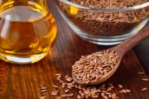 Brown flax seeds on spoon and flaxseed oil in glass jug on wooden table. Flax oil is rich in omega-3 fatty acid.