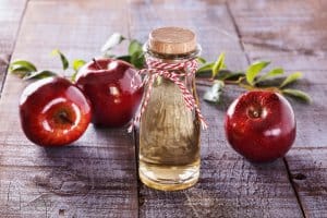 Apple cider vinegar and red apples over rustic wooden background