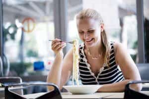 Lifestyle portrait of a young woman eating hot spaghetti and smiling. Focus is on the fork with spaghetti