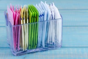 Packets of artificial sweeteners in glass container sitting on bright blue wooden table