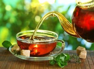 Pouring tea from a teapot into a cup on a blurred background of nature showing omad diet liquid