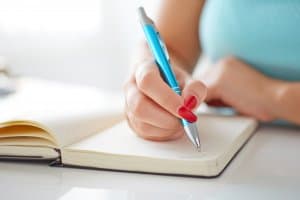 Young woman writes to black diary on a white table