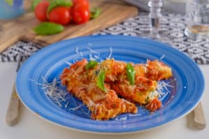 cannelloni pasta dish with tomatoe sauce on a blue plate with tomatoes in the background and wine