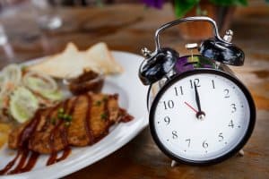 Clock on Wooden Table with steak on background, Lunch Time Concept