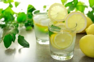 Lemon water with fresh lemons and green plants