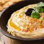 A bowl of creamy hummus with olive oil and pita chips.