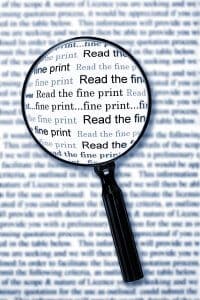 Magnifying glass over document, highlighting the words "read the fine print". Cyan toned image.