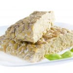 Yellow tempeh served on plate with edamame.